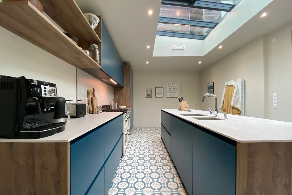 The finished kitchen extension: blue handleless units, a long island, patterned floor tiles and a glazed rooflight.