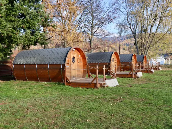 A row of barrel-shaped wooden huts with decks on a sunny autumn lawn