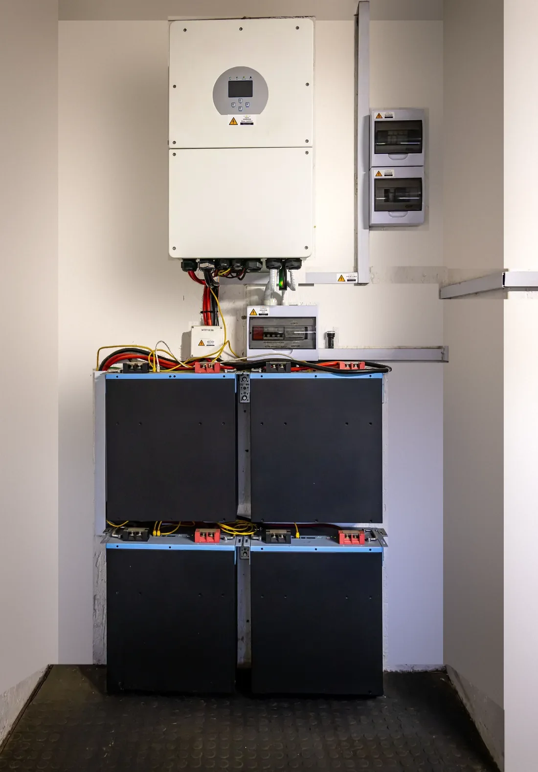 A white hybrid inverter and four black battery modules installed neatly in a utility room