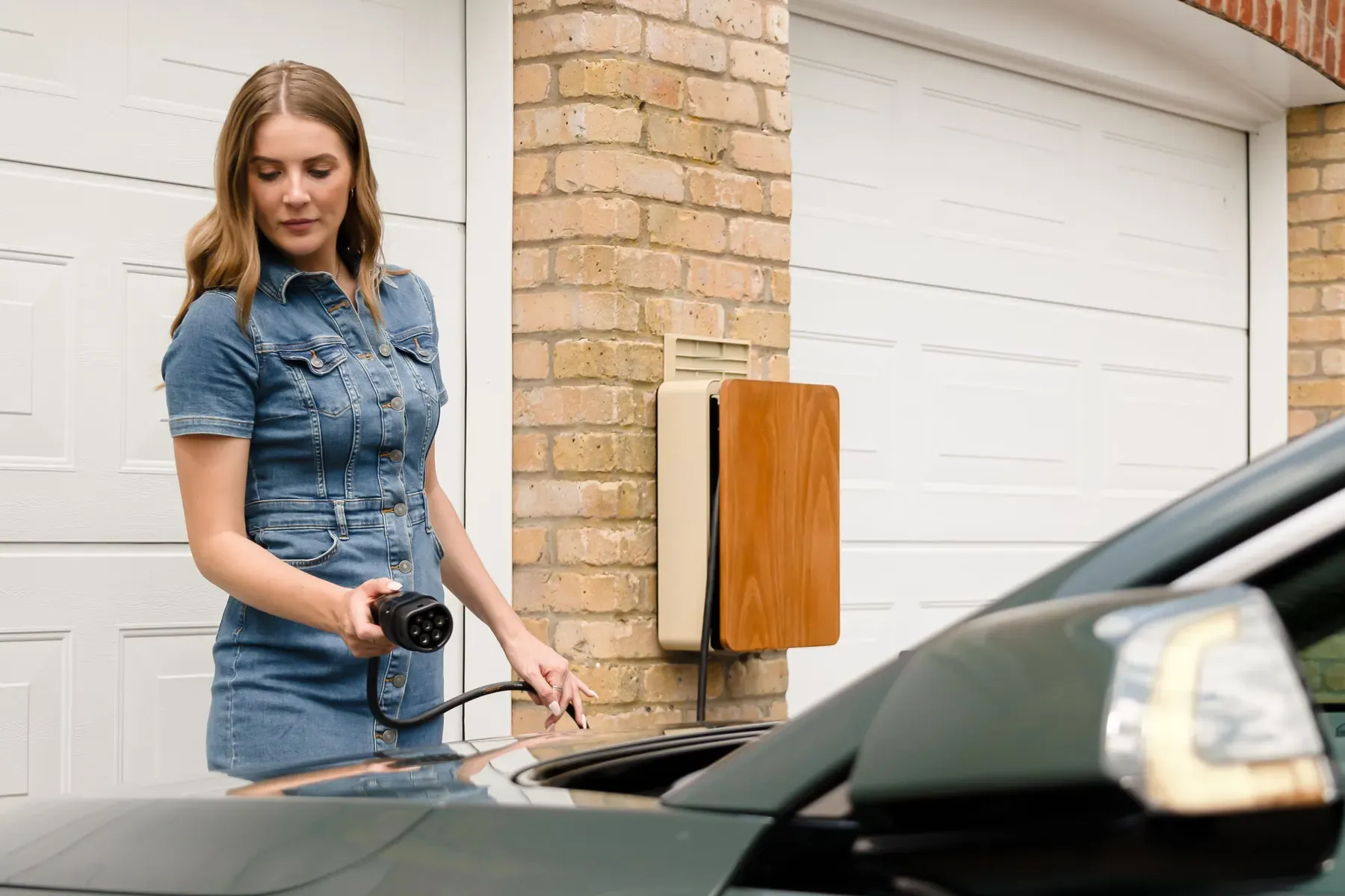 A woman plugging a charging cable into an electric car next to a wall-mounted home charger