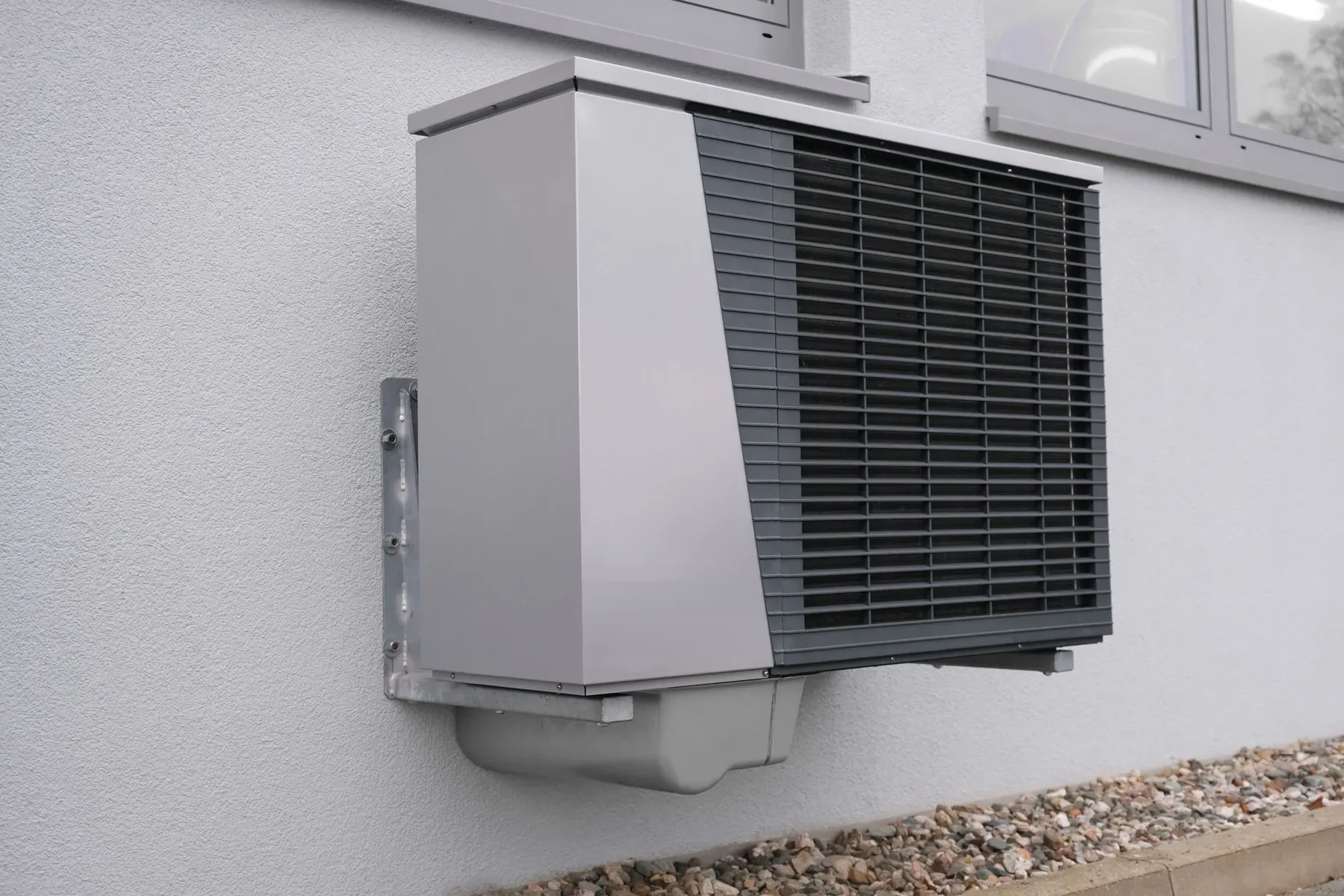 A grey air source heat pump mounted on the outside wall of a house
