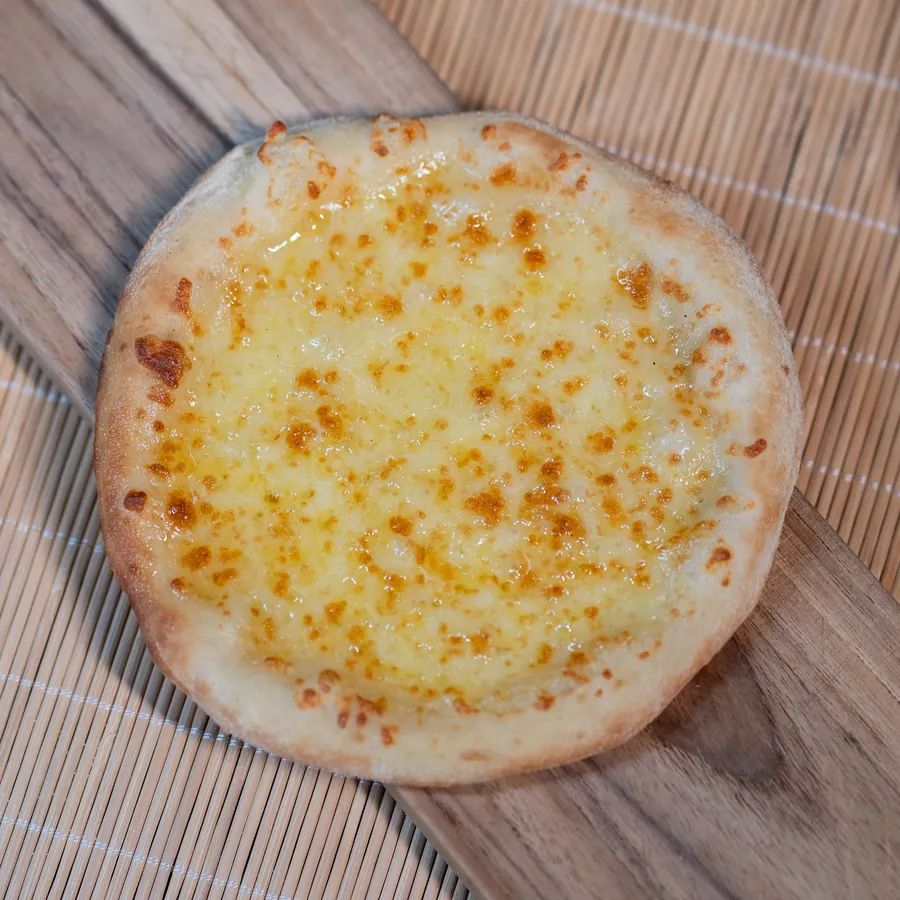 A wood-fired cheese pizza on a wooden board, seen from above.